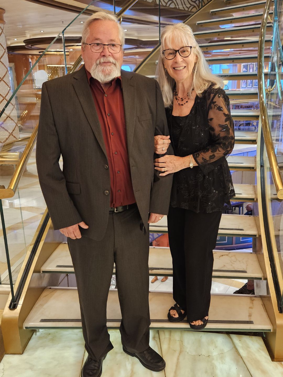 A well-dressed couple standing together on an elegant staircase, sharing a proud and joyful moment during a special occasion.