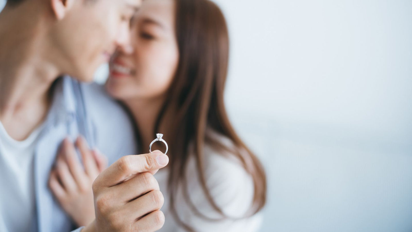 A couple sharing an intimate moment while holding a diamond engagement ring in focus, symbolizing a marriage proposal.