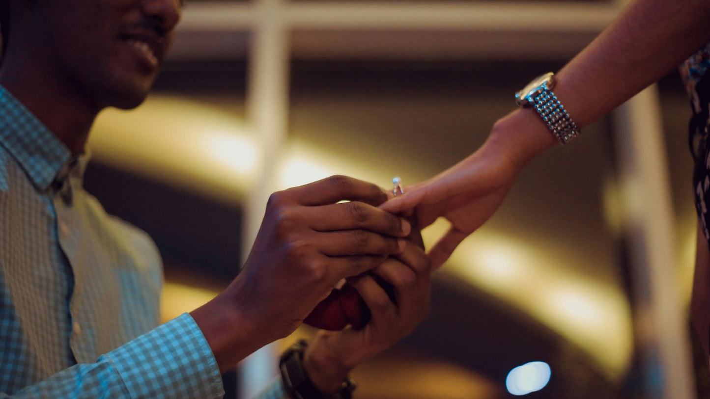 A close-up of a person placing a diamond engagement ring on their partner’s finger during a romantic proposal.