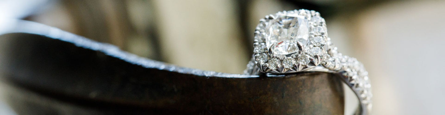 Close-up of a diamond engagement ring with a cushion-cut center stone and halo setting, resting on a dark sculptural surface for a dramatic, elegant look.