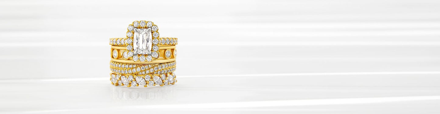 Stacked yellow gold diamond wedding bands with an emerald-cut halo engagement ring, featuring pavé and marquise diamond detailing on a clean white background.