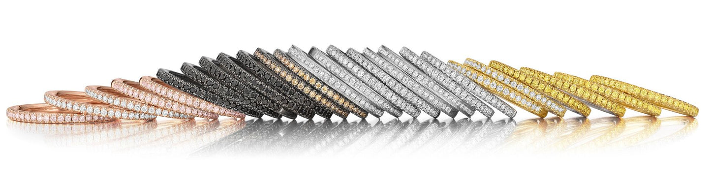 Collection of slim pavé diamond wedding bands in rose gold, black gold, white gold, and yellow gold arranged in a gradient display.