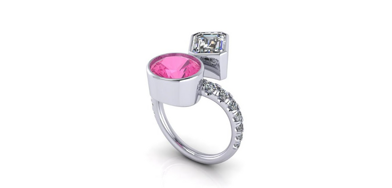 A contemporary white gold open shank bypass ring featuring a bezel set round pink sapphire and an emerald cut diamond from a custom jewelry creator